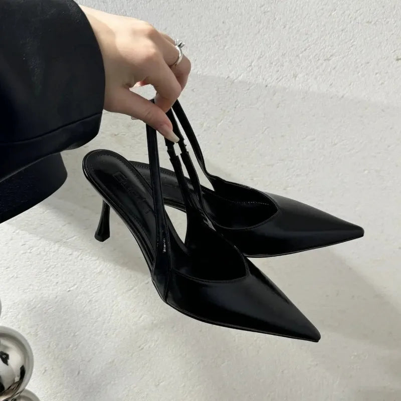 Black high-heeled shoes being held by a hand on a light gray background