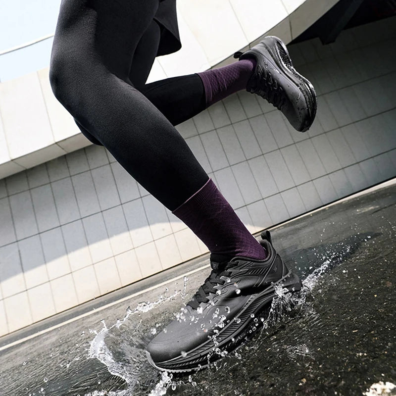 A person running through shallow water outdoors, wearing black athletic shoes, black leggings, and dark purple crew socks.