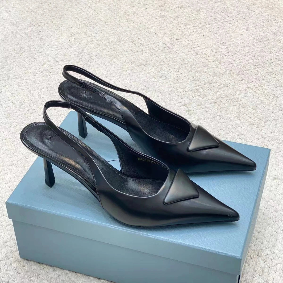 Black high-heeled shoes on a light blue box with a textured white background