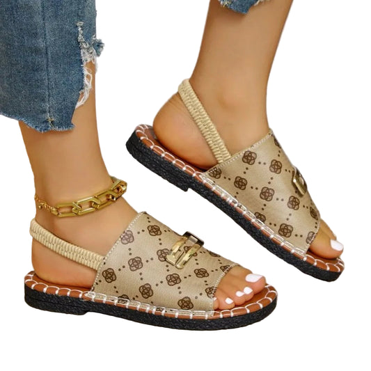 Beige sandals with brown floral pattern worn by a person sitting on a woven chair.