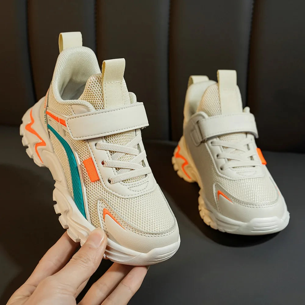 Beige children's sneakers with colorful accents held by a hand against a dark background