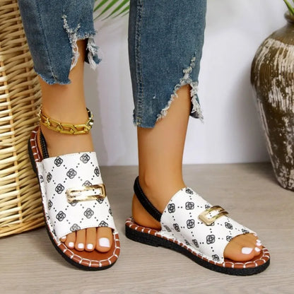 White sandals with black patterns and gold buckles worn by a person with ripped jeans.
