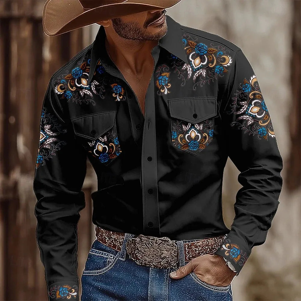 Man wearing a black embroidered shirt with floral patterns, blue jeans, and a cowboy hat.