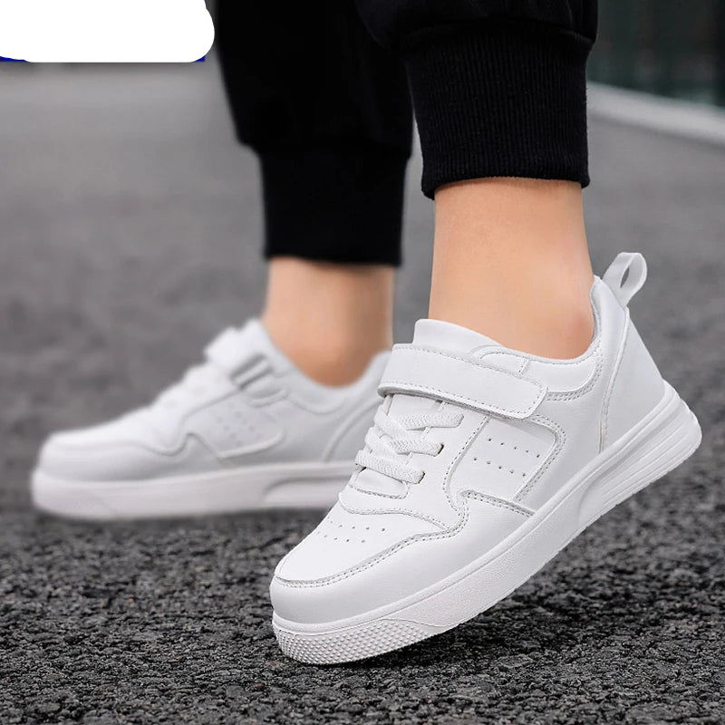 White NBGAGA low-top sneakers with hook-and-loop straps and laces, shown on a person standing on gray asphalt.