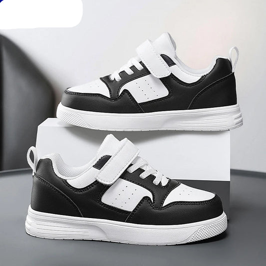 A pair of NBGAGA kids' low-top sneakers in black and white, featuring hook-and-loop straps and thick white soles, displayed on a white block against a gray background.