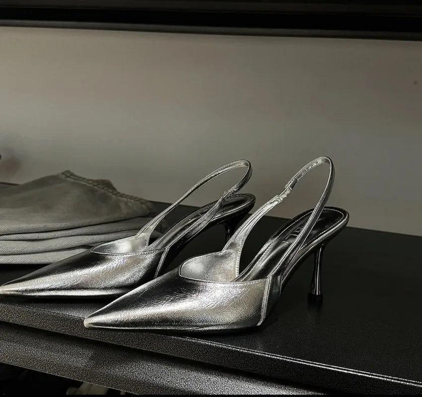 Pair of silver high-heeled shoes on a dark surface with a neutral background
