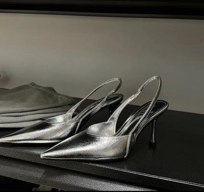Pair of silver high-heeled shoes on a dark surface with a neutral background