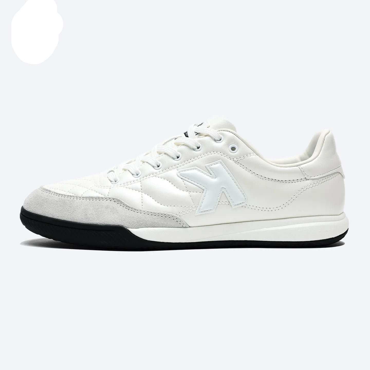 A white low-top sneaker by Kelme, featuring a white leather and suede upper, a white side logo, white laces, and a black outsole, shown against a light gray background with the Kelme logo in the top-left corner.