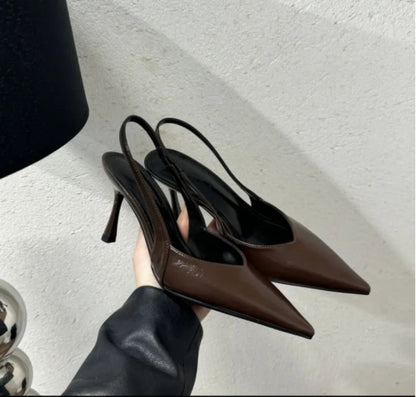 Pair of brown high-heeled shoes held by a hand on a light background