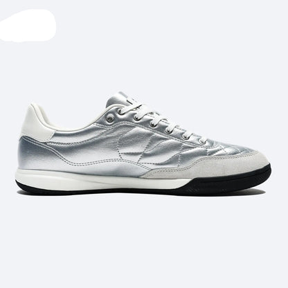 A silver and white low-top sneaker by KELME, featuring a metallic silver upper, white laces, a white midsole, and a black outsole, shown from a side profile on a light gray background.