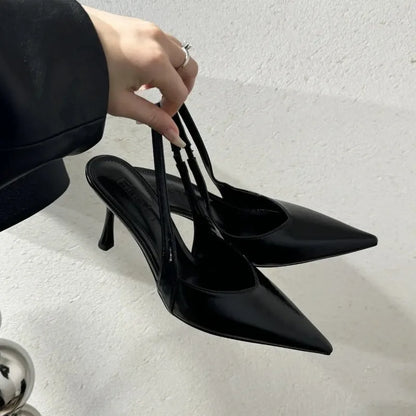 Black high-heeled shoes being held by a hand on a light gray background