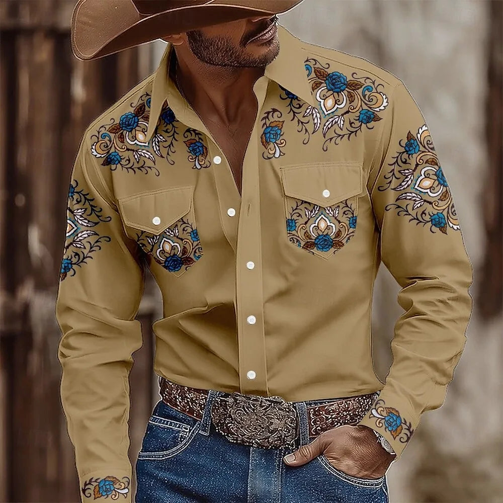 Man wearing a beige embroidered shirt with blue floral patterns, blue jeans, and a brown cowboy hat.