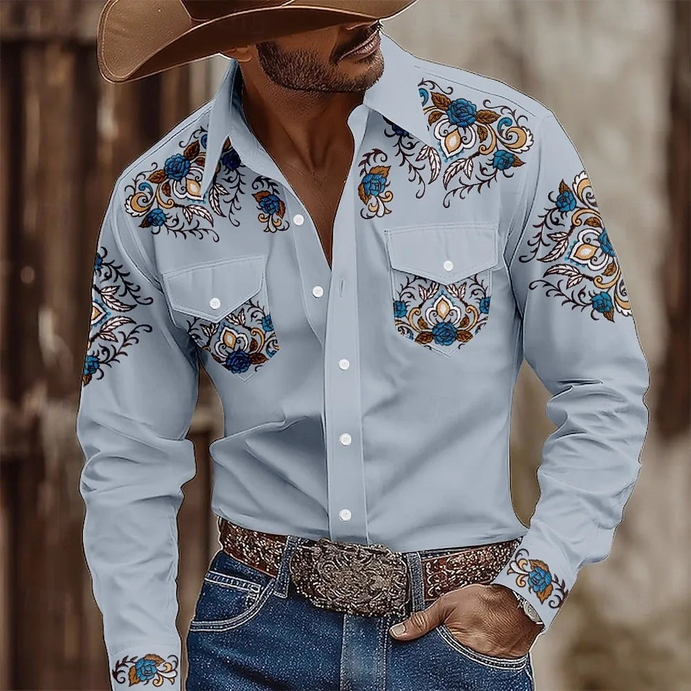 Man wearing a light blue embroidered shirt with decorative patterns, paired with jeans and a brown hat.