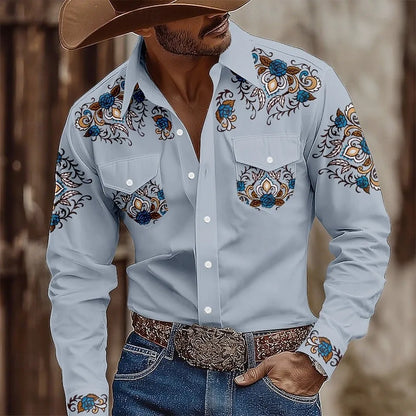 Man wearing a light blue embroidered shirt with decorative patterns, paired with jeans and a brown hat.