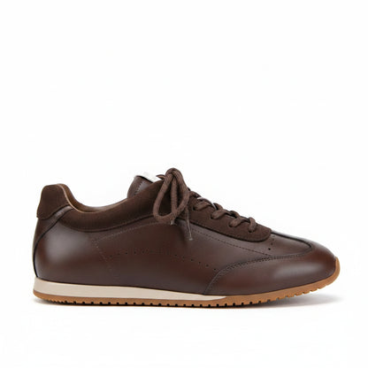 A dark brown genuine leather sneaker held by a hand against a beige carpet background, with text overlays reading 'GENUINE LEATHER' and 'NATURAL LEATHER, COWHIDE, HANDMADE'.