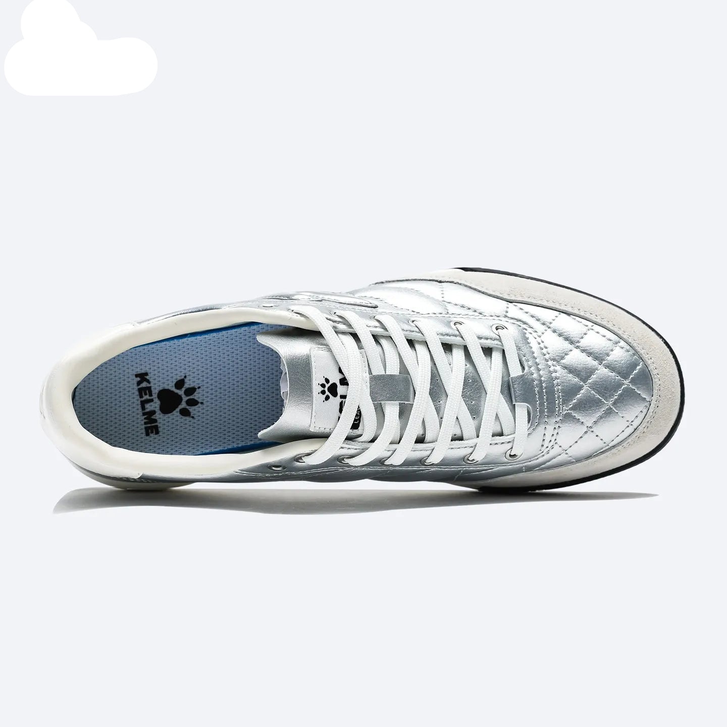 A silver quilted sneaker with white laces, shown from a side profile view on a light gray background. The KELME brand logo is visible on the tongue and inlay of the heel.