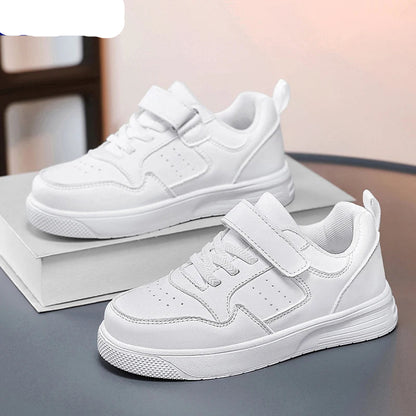 A pair of white NBGAGA low-top sneakers with hook-and-loop straps, displayed on a gray surface with a white book prop.
