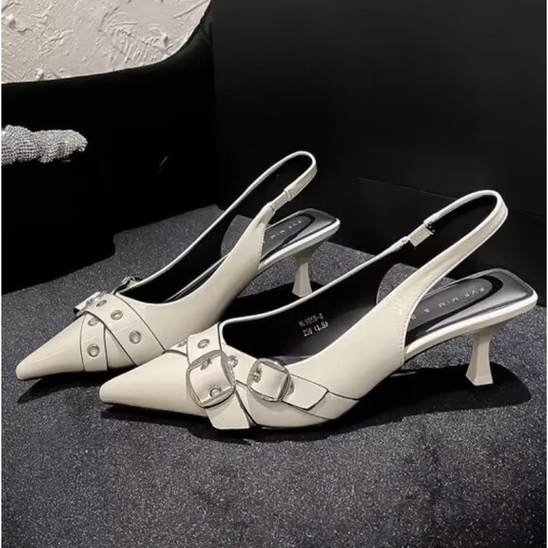 Pair of white kitten heel shoes with buckles on a dark surface