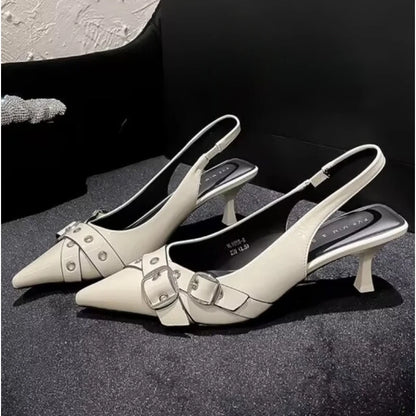 Pair of white kitten heel shoes with buckles on a dark surface