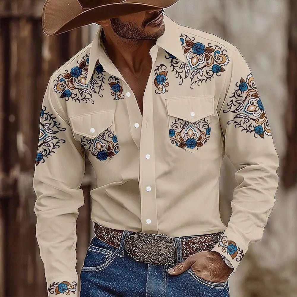 Man wearing a beige embroidered shirt with blue floral patterns, blue jeans, and a brown hat.