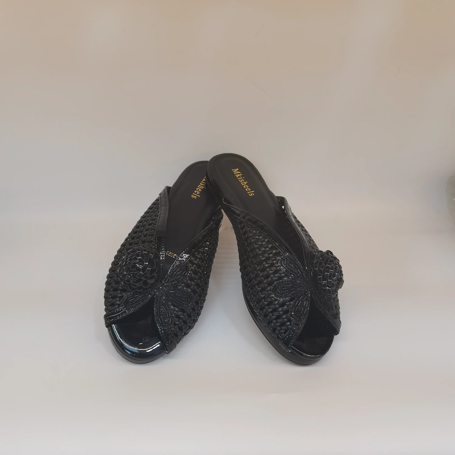Pair of black open-toe shoes with woven design on a light beige background