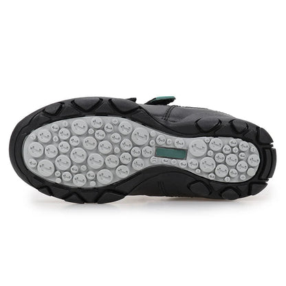 A black UOVO shoe shown from the sole view, featuring a textured black rubber outsole with circular tread patterns and a small green accent tab, on a white background.