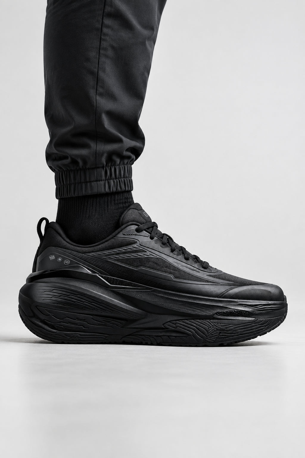 A black athletic sneaker shown at an angle on a light gray textured background with promotional text reading 'QIAODAN' and 'ANTI SLIP AND STABLE LIKE A ROCK,' plus a black bird graphic and 'SLIP-RESISTANT AND WEAR-RESISTANT' badge.