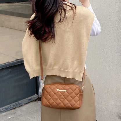 Person wearing a beige sweater vest and holding a brown quilted handbag.