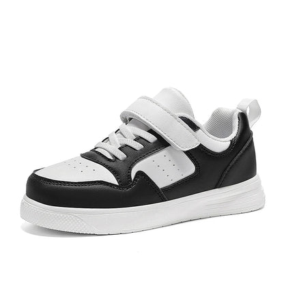 A black and white low-top sneaker with a hook-and-loop strap closure, white laces, and a thick white sole, shown from a side profile on a white background.
