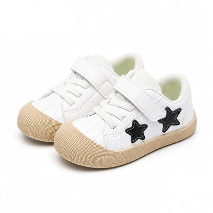 A pair of toddler low-top sneakers by PmwRun in white, featuring black star-shaped patches on the sides, white laces, hook-and-loop straps, and textured beige rubber soles. The brand logo 'PmwRun' is visible in the top left, and the color name 'Black' is in the bottom right.