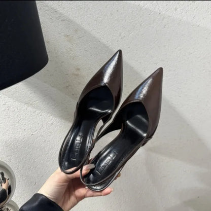 Pair of black high-heeled shoes held by a hand on a light-colored floor.